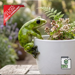 Puede incluir: Una figura de rana verde brillante posada en una maceta de cerámica blanca llena de vegetación y pequeñas flores blancas. La rana tiene ojos negros y se aferra al borde de la maceta. Una pancarta roja dice "3D STL FILES DIGITAL DOWNLOAD".