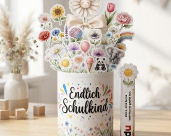 Op de afbeelding: Een cilindervormige witte houder met de tekst Endlich Schulkind en kleurrijke bloemenillustraties. Het bevat een boeket van papieren uitsparingen met bloemen, een panda, een olifant en een regenboog. Een klein rechthoekig label met een madeliefje is bevestigd.