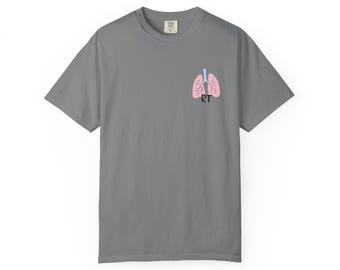 Könnte beinhalten: Ein graues Kurzarm-T-Shirt mit einer kleinen Grafik auf der oberen linken Brustseite. Die Grafik zeigt ein Paar hellrosa menschliche Lungen mit einer hellblauen Luftröhre und Bronchien, darunter sind die schwarzen Großbuchstaben RT gedruckt.