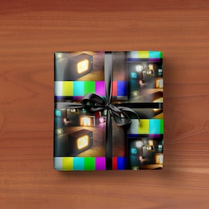 May include: A wrapped gift with a black ribbon and bow. The wrapping paper features a repeating pattern of retro televisions with glowing screens and colorful test patterns. The gift is on a wooden surface.