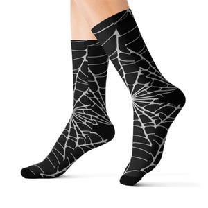 May include: Black socks with a white spiderweb design. The socks are knee-high and feature a detailed web pattern. The design is centered on the front of the socks, creating a striking visual effect. These socks are a unique accessory.