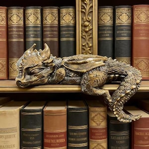 Könnte beinhalten: Eine bronzefarbene Drachenfigur, mit detaillierten Schuppen und Flügeln, ruht auf einem Regal. Das Regal ist mit antiken Büchern mit goldenen Details und verschiedenfarbigen Buchrücken ausgekleidet, was eine Vintage-Ästhetik erzeugt.