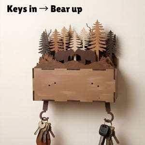 May include: Wooden key holder with a forest scene featuring two bears and trees. The key holder has a rectangular box with two hooks for keys. The text "Keys in -> Bear up" is at the top.