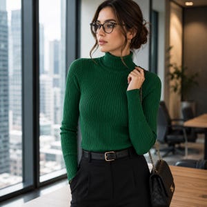 Könnte beinhalten: Ein dunkelgrüner, gerippter Rollkragenpullover mit langen Ärmeln, kombiniert mit einer schwarzen Hose und einem schwarzen Ledergürtel mit goldener Schnalle. Eine schwarze, gesteppte Umhängetasche mit goldener Kette wird über der Schulter getragen.