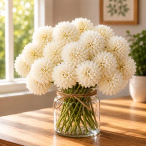 May include: A bouquet of cream-colored, spherical chrysanthemum flowers arranged in a clear glass jar. The stems are tied with a thin, brown twine wrapped around the neck of the jar, showcasing green stalks visible through the transparent glass.