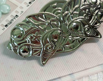 Könnte beinhalten: Eine silberfarbene Haarspange aus Metall mit einem komplexen, geprägten Schmetterlingsflügel-Design, Wirbelmustern, kreisförmigen Akzenten und kleinen Sternformen. Ein weißes Maßband zeigt eine Länge von etwa 7,5 cm an.