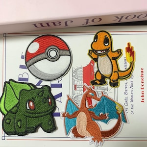 May include: Embroidered patches featuring a red and white Pokéball, a green Bulbasaur, an orange Charmander, and an orange and blue Charizard. The patches are on a book with the text "book of jam".
