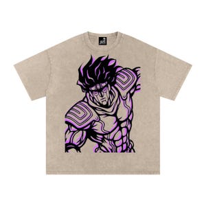 May include: Tan t-shirt featuring a stylized illustration of a muscular figure with black and purple accents. The graphic is centered on the front of the shirt. The shirt has a crew neck and short sleeves.
