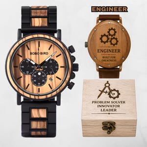 May include: A Bobo Bird wristwatch with a wood grain face, black metal and wood link band, and three sub-dials. Beside it, a watch back engraved with three gears and the text ENGINEER BUILT FOR GREATNESS, and a wooden box labeled PROBLEM SOLVER INNOVATOR LEADER.