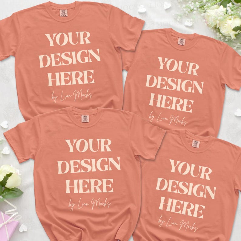 Puede incluir: Cuatro camisetas de manga corta de color coral dispuestas en grupo. Cada camiseta presenta el texto blanco "YOUR DESIGN HERE" en una fuente serif en negrita, seguido del texto en cursiva "by Lion Mocks" y una peque&ntilde;a etiqueta rectangular en el cuello.