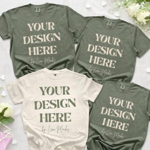 Puede incluir: Tres camisetas de manga corta en colores verde oliva y crema. Cada camiseta presenta el texto "YOUR DESIGN HERE" en una fuente serif negrita, seguido de la escritura cursiva "by Lion Mocks" impresa en el centro de la prenda.