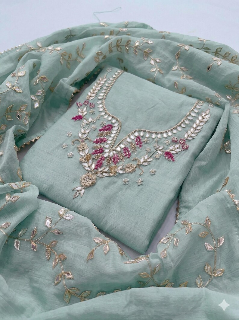 May include: A light teal-colored embroidered salwar kameez set. The top features intricate embroidery with silver and pink accents around the neckline. The matching dupatta is adorned with similar leaf-shaped embroidery.