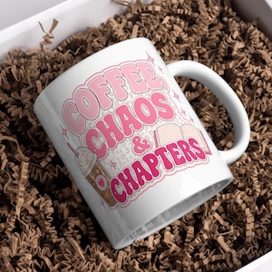 Peut inclure: Mug en céramique blanche avec l'inscription "COFFEE, CHAOS & CHAPTERS" en lettres roses. La tasse présente une illustration d'une boisson au café et d'un livre. La tasse est emballée dans une boîte blanche avec du papier brun.