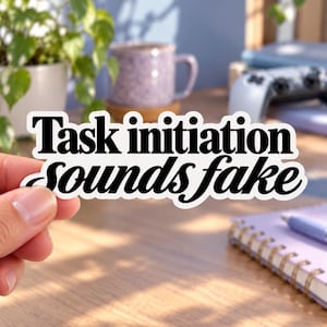 Pode incluir: Um adesivo de vinil cortado com borda branca e texto preto que diz Task initiation sounds fake. O adesivo apresenta uma combinação de uma fonte serifada em negrito para as duas primeiras palavras e uma fonte cursiva para as duas últimas.