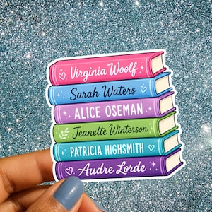 Op de afbeelding: Een sticker met een stapel van zes kleurrijke boeken met witte ruggen en tekst. De boeken zijn gelabeld met de namen Virginia Woolf, Sarah Waters, Alice Oseman, Jeanette Winterson, Patricia Highsmith en Audre Lorde, versierd met kleine sterretjes en hartjes.