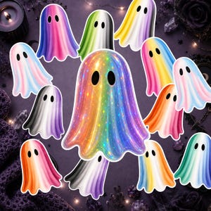 Puede incluir: Una colección de pegatinas con forma de fantasma que presentan varios degradados de color, incluido un gran fantasma arcoíris holográfico central con detalles de estrellas. Cada fantasma tiene dos ojos ovalados negros y una silueta sencilla.