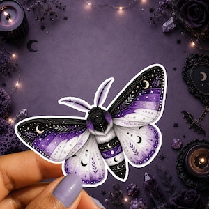 May include: A die-cut sticker featuring a moth with a purple and white gradient colour scheme. The wings and body are decorated with celestial motifs including crescent moons, stars, and leafy patterns, rendered in black, white, and purple.