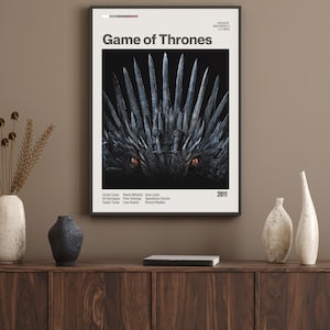 Puede incluir: Un póster enmarcado con el título "Game of Thrones" en texto blanco. La imagen muestra un primer plano del Trono de Hierro con ojos naranjas. El póster incluye el año 2011 y los nombres de los miembros del reparto.