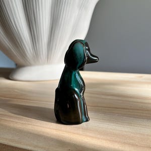 May include: A small, ceramic duck figurine in teal and brown. The duck is sitting upright with its head turned. A large, white, shell-shaped decorative piece is in the background.