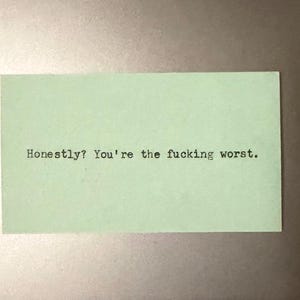 May include: A pale green rectangular card with the text "Honestly? You're the fucking worst." printed in black. The card is centered and the text is in a typewriter-style font.