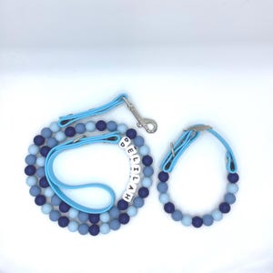 May include: A blue dog collar and lead set. The lead has a silver clasp and a handle. The collar and lead are made of blue beads in various shades, with the name "DELILAH" spelled out on the collar.