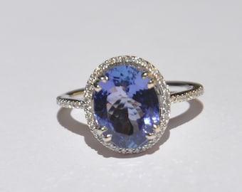 Op de afbeelding: Een zilveren ring met een grote ovale blauwe edelsteen omringd door een halo van kleinere diamanten.
