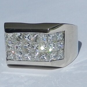 May include: A silver ring with a rectangular band set with multiple rows of small, square-shaped diamonds.