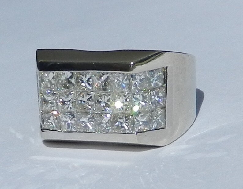 May include: A silver ring with a rectangular band set with multiple rows of small, square-shaped diamonds.