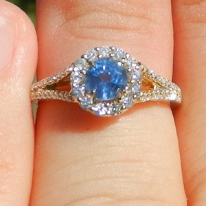 Op de afbeelding: Een gouden ring met een blauwe saffier in het midden, omringd door een halo van kleinere diamanten.