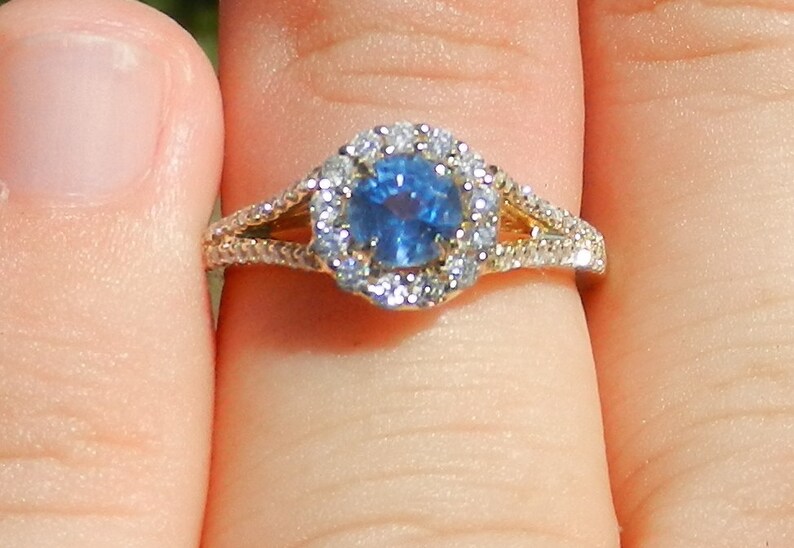 Op de afbeelding: Een gouden ring met een blauwe saffier in het midden, omringd door een halo van kleinere diamanten.