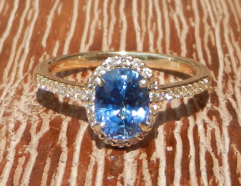 May include: A gold ring with a blue oval gemstone surrounded by a halo of smaller diamonds. The ring has a delicate band with a row of diamonds.