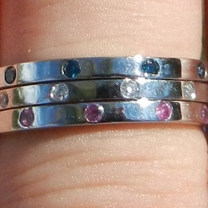 Pu&ograve; includere: Un anello d'argento con tre bande, ciascuna con piccole pietre preziose. La banda superiore &egrave; incastonata con pietre blu, la banda centrale con pietre bianche e la banda inferiore con pietre rosa.
