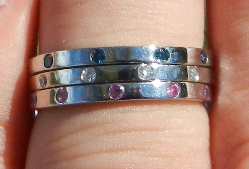 Pu&ograve; includere: Un anello d'argento con tre bande, ciascuna con piccole pietre preziose. La banda superiore &egrave; incastonata con pietre blu, la banda centrale con pietre bianche e la banda inferiore con pietre rosa.