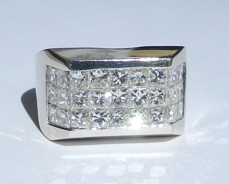 May include: A silver ring with a wide band set with multiple rows of square-cut diamonds.