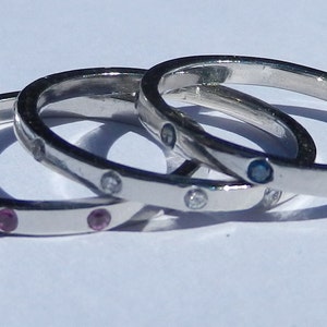Pu&ograve; includere: Tre anelli d'argento con pietre preziose di diversi colori. L'anello superiore ha pietre blu, l'anello centrale ha pietre bianche e l'anello inferiore ha pietre rosa.
