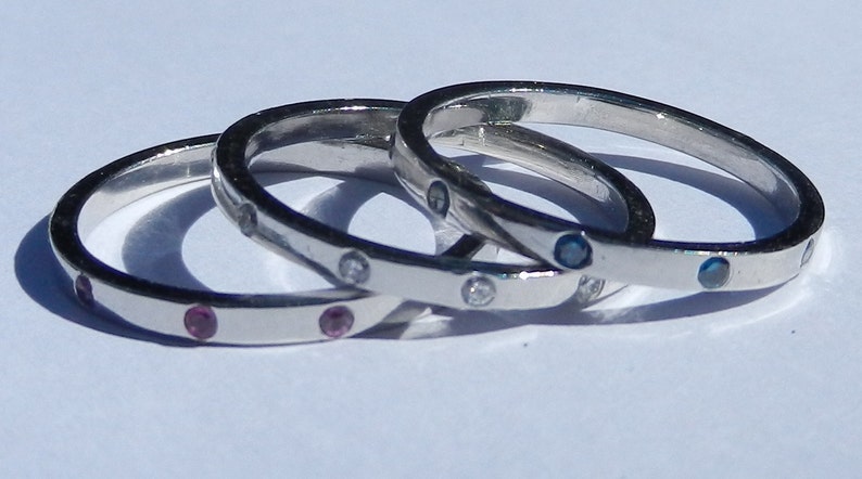 Pu&ograve; includere: Tre anelli d'argento con pietre preziose di diversi colori. L'anello superiore ha pietre blu, l'anello centrale ha pietre bianche e l'anello inferiore ha pietre rosa.