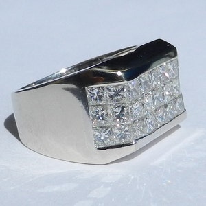 May include: A silver men's ring with a square-shaped band and a row of small, clear, square-cut diamonds.
