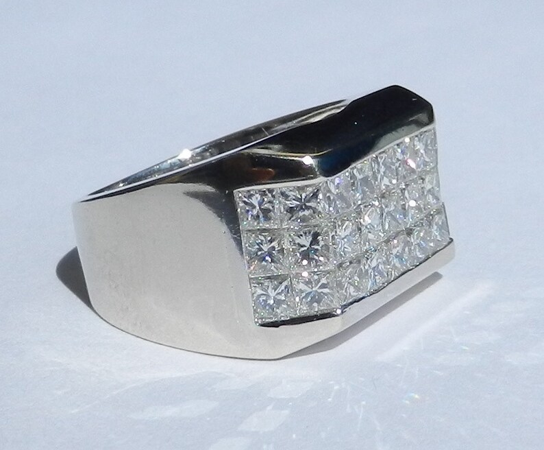 May include: A silver men's ring with a square-shaped band and a row of small, clear, square-cut diamonds.