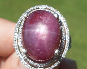 Op de afbeelding: Een zilveren ring met een grote, ovale, roze ster-robijn, omgeven door een dubbele halo van kleine diamanten.