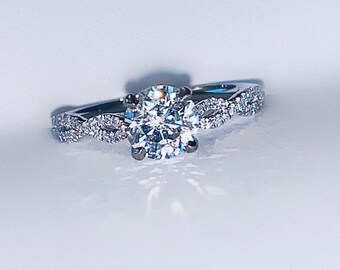 May include: A silver engagement ring with a large, round, clear diamond center stone. The band is set with smaller diamonds in a twisted design.