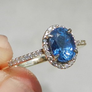 May include: A gold ring with a large oval blue sapphire surrounded by a halo of smaller diamonds. The ring has a band of smaller diamonds.