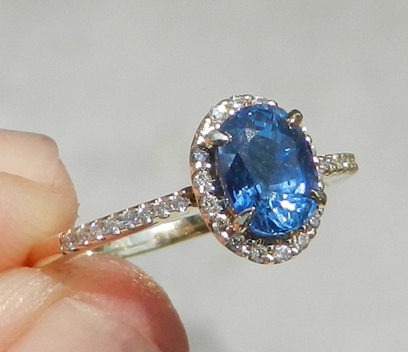 May include: A gold ring with a large oval blue sapphire surrounded by a halo of smaller diamonds. The ring has a band of smaller diamonds.