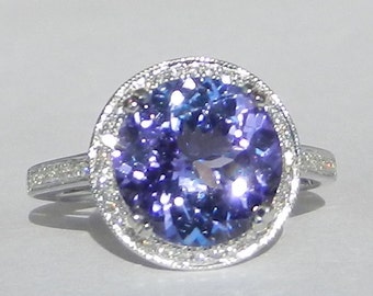 Op de afbeelding: Een zilveren ring met een grote, ronde, paarse edelsteen omringd door een halo van kleinere diamanten.