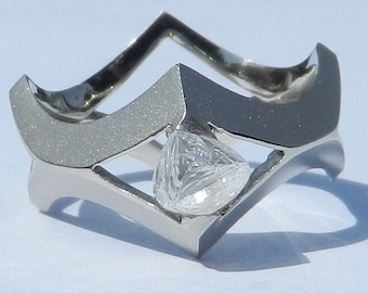 May include: A silver ring with a unique, geometric design. The ring features a large, clear, faceted gemstone in the center.