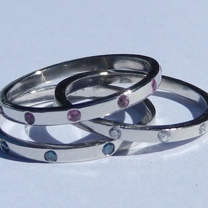 Pu&ograve; includere: Tre anelli d'argento con pietre preziose di diversi colori. L'anello superiore ha pietre preziose rosa, l'anello intermedio ha pietre preziose blu e l'anello inferiore ha pietre preziose trasparenti.