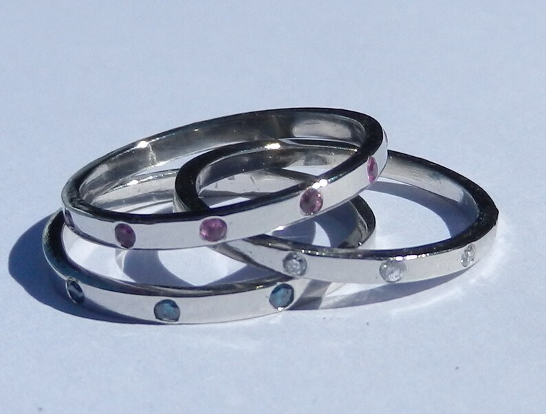 Pu&ograve; includere: Tre anelli d'argento con pietre preziose di diversi colori. L'anello superiore ha pietre preziose rosa, l'anello intermedio ha pietre preziose blu e l'anello inferiore ha pietre preziose trasparenti.