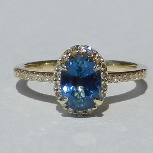 May include: A gold ring with a blue oval gemstone surrounded by a halo of smaller diamonds. The band is also set with smaller diamonds.