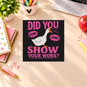 Könnte beinhalten: Ein quadratischer Grafikdruck auf schwarzem Hintergrund mit einer weißen Gans mit orangefarbenen Füßen und Schnabel. Der Text DID YOU HONK! HONK! SHOW YOUR WORK? ist in leuchtendem Pink gehalten, wobei die Gans mittig platziert ist.