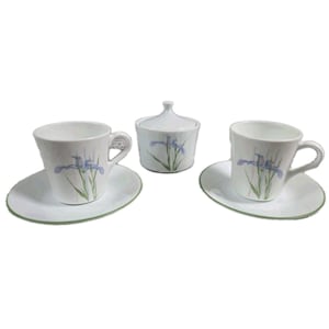 Peut inclure: Un service à thé en céramique blanche composé de deux tasses avec soucoupes assorties et d'un sucrier avec couvercle. Chaque pièce présente une illustration botanique délicate d'iris violet avec des tiges et feuilles vertes, bordée d'un fin liseré vert.