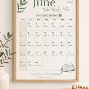 Può includere: Un calendario incorniciato del Piano di lettura della Bibbia di giugno 2026 con una cornice in legno chiaro. Il calendario presenta un design minimalista con una foglia ad acquerello e il testo: "30 giorni nella parola di Dio". Libri e un vaso in primo piano.